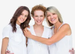 Three smiling women posing closely together in white tops.