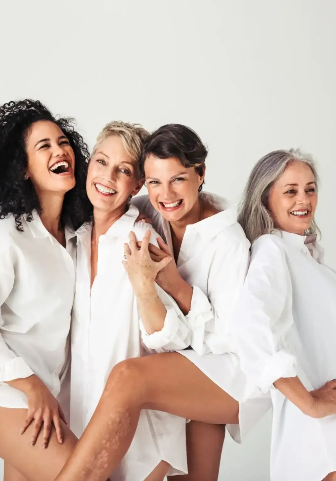 Four joyful women in white shirts celebrating together.