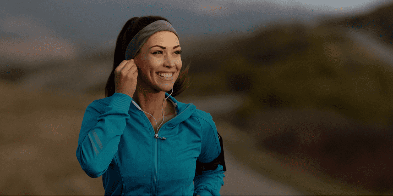 Smiling woman jogging with headphones outdoors.