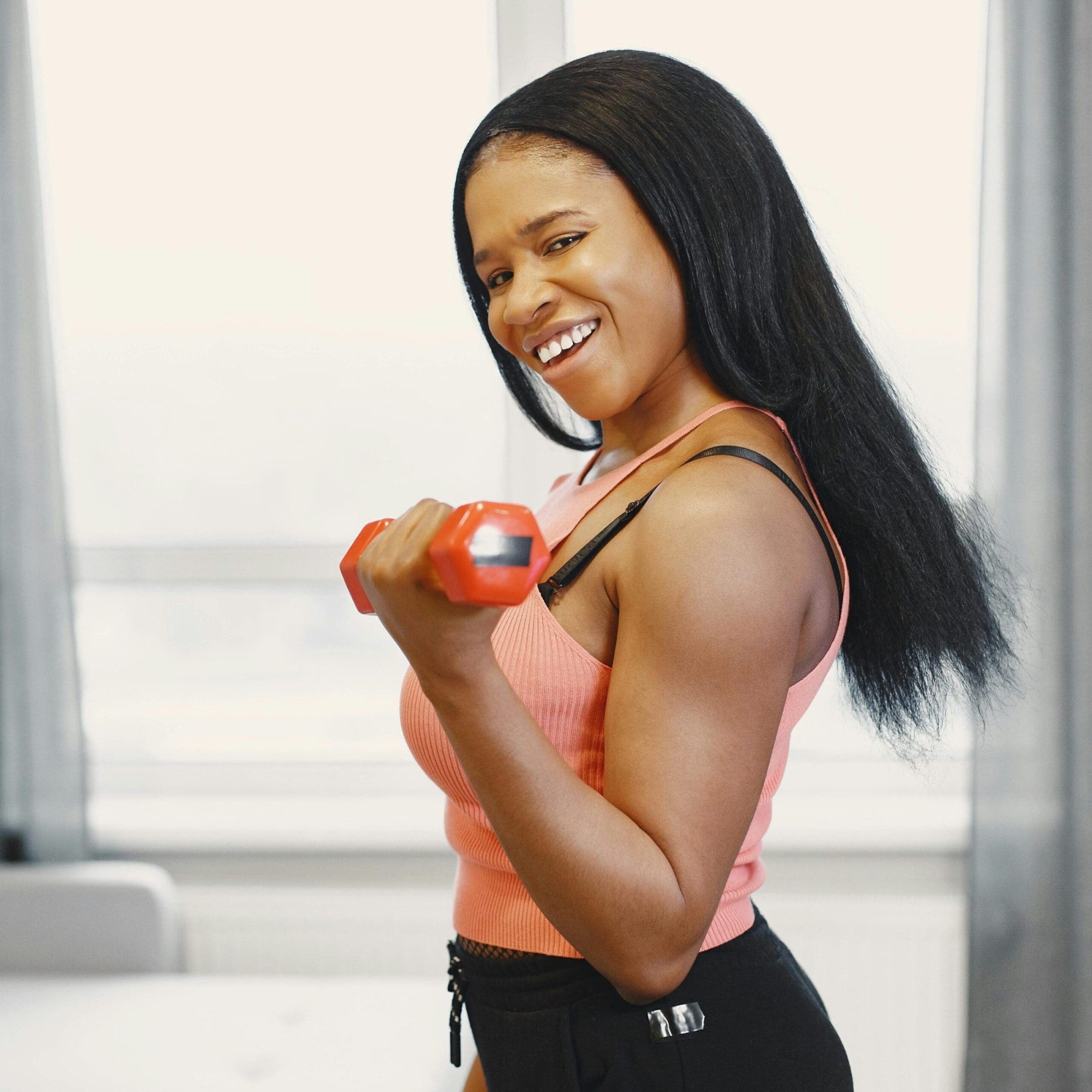 Woman smiling while lifting a dumbbell indoors.