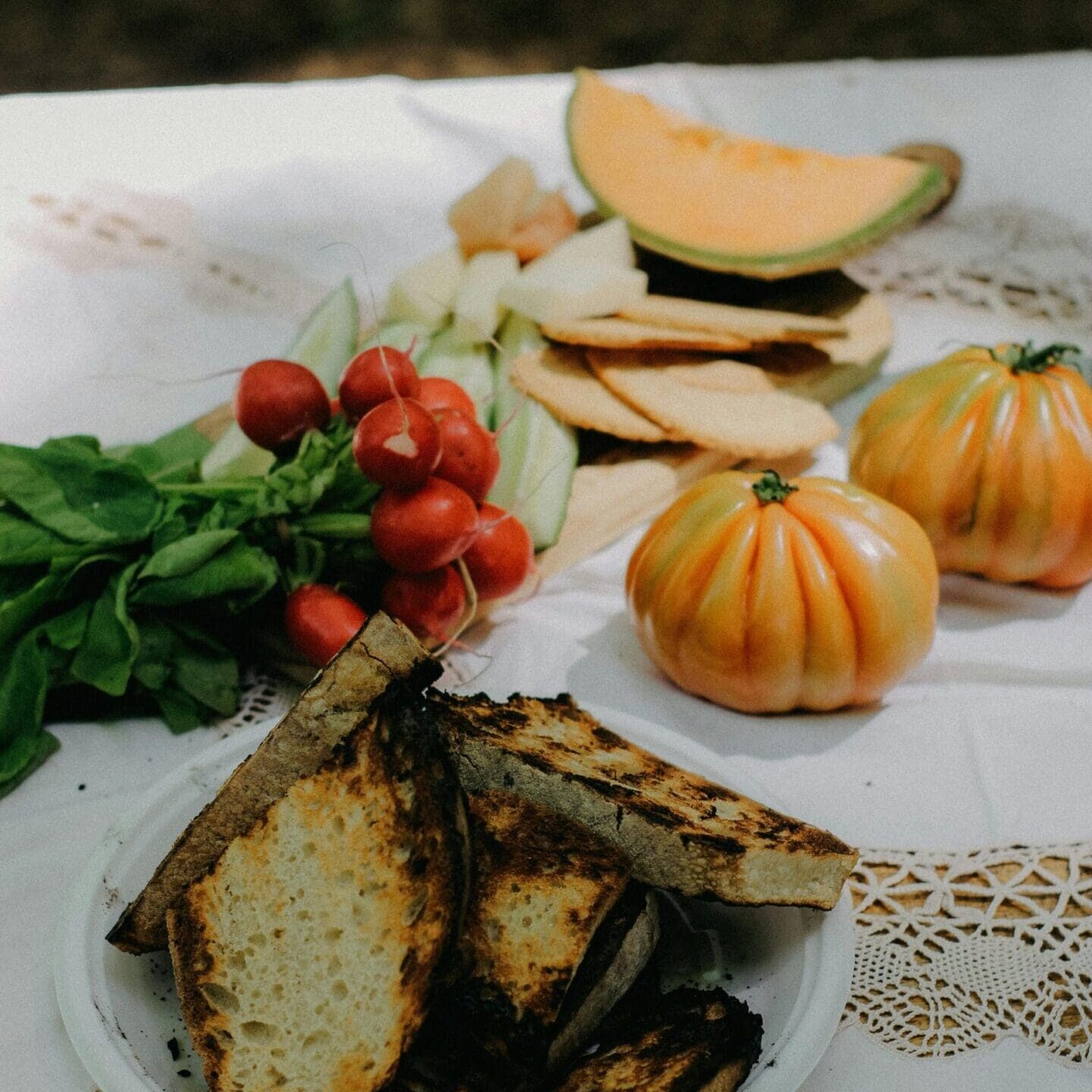 Fresh produce and bread on lace tablecloth.